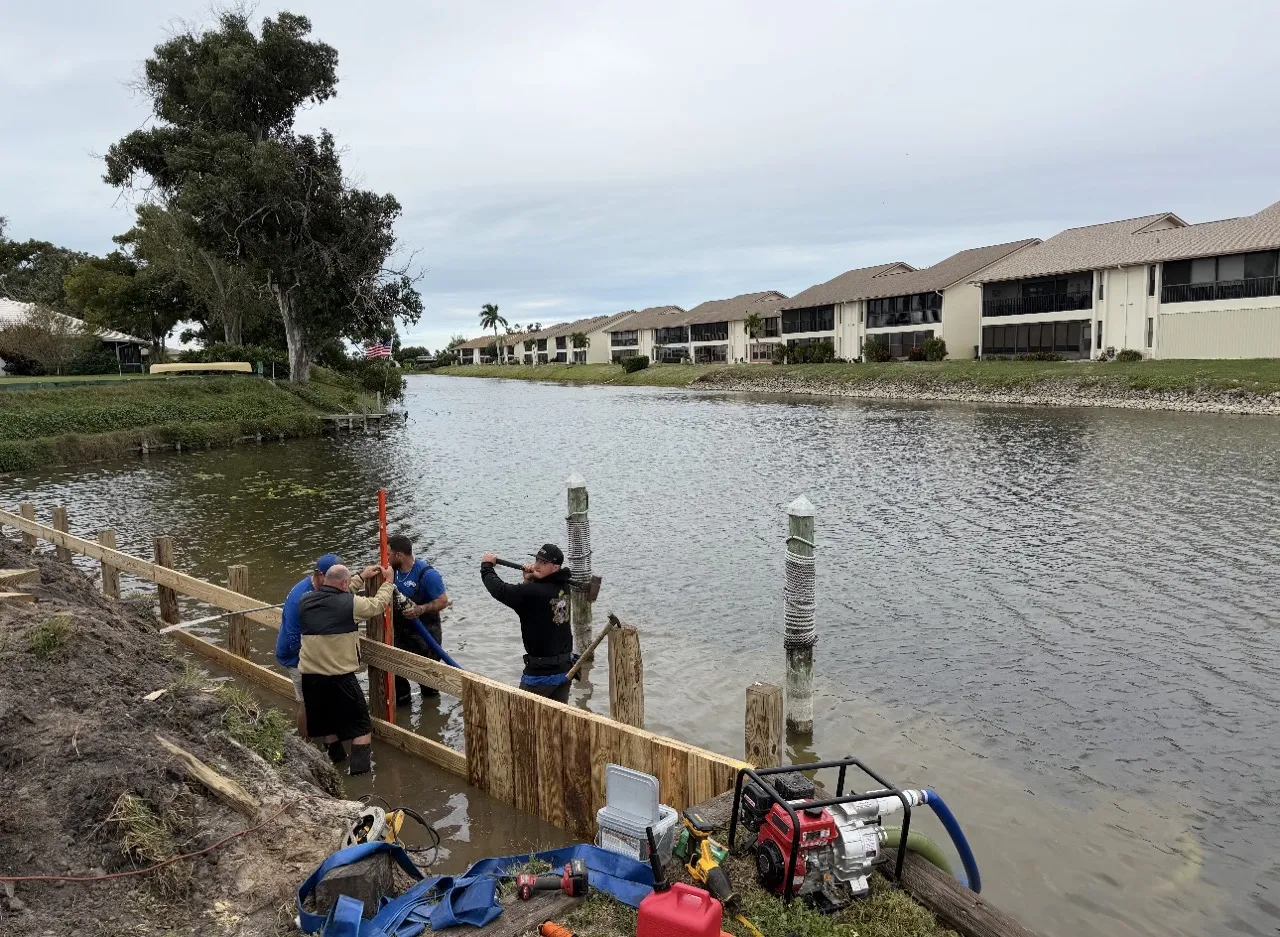 Crew aligning new bulkhead posts along a canal lined with condos