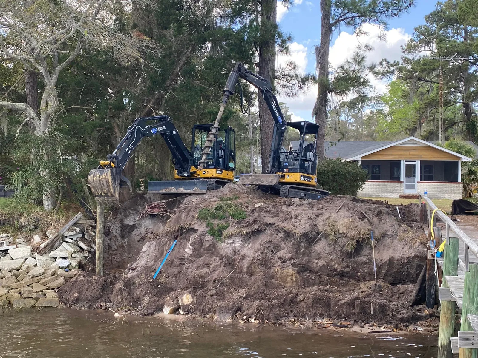 Excavator working on an eroded waterfront bank beside a home