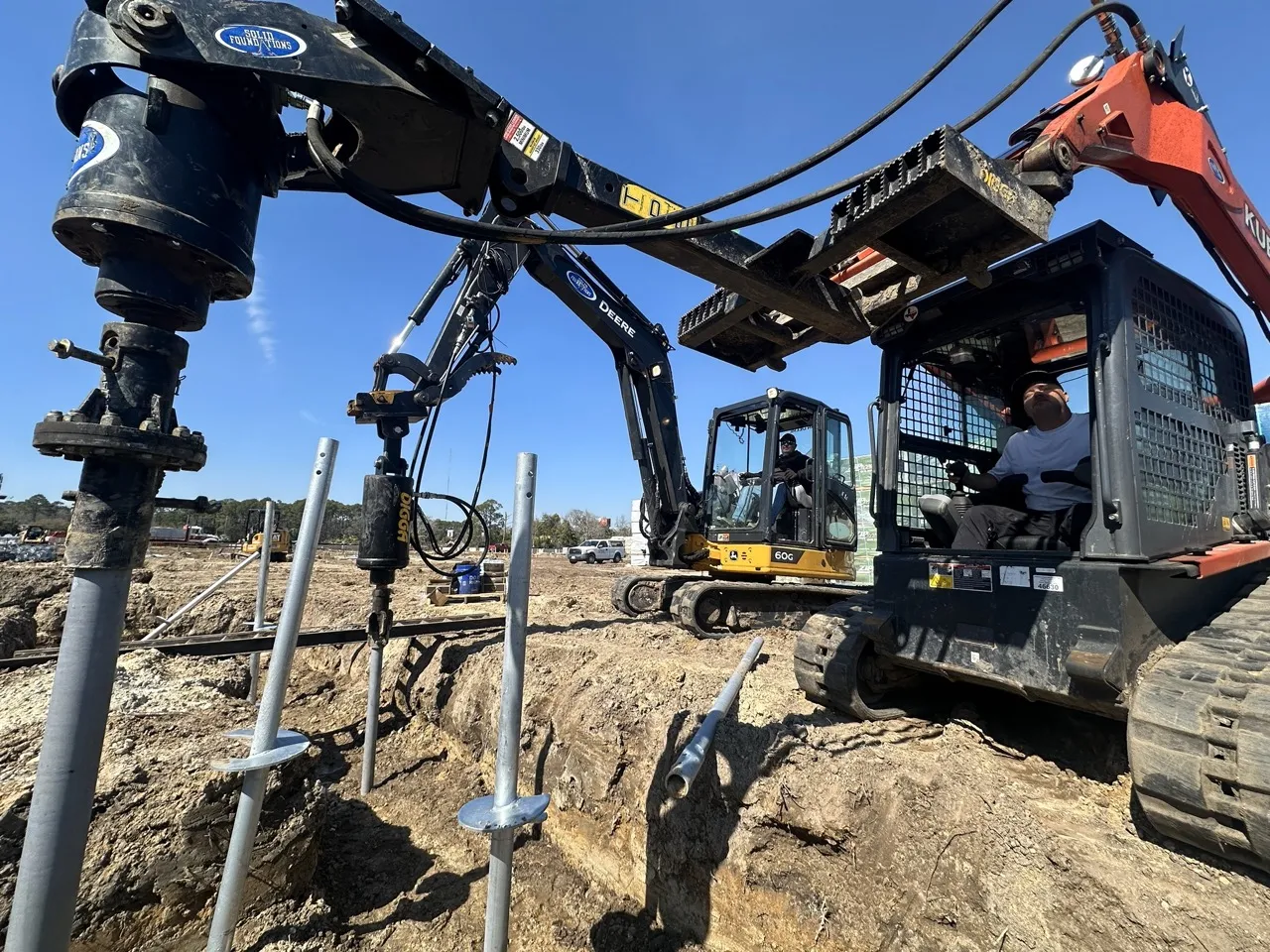 Helical pier being driven by an excavator-mounted drive head