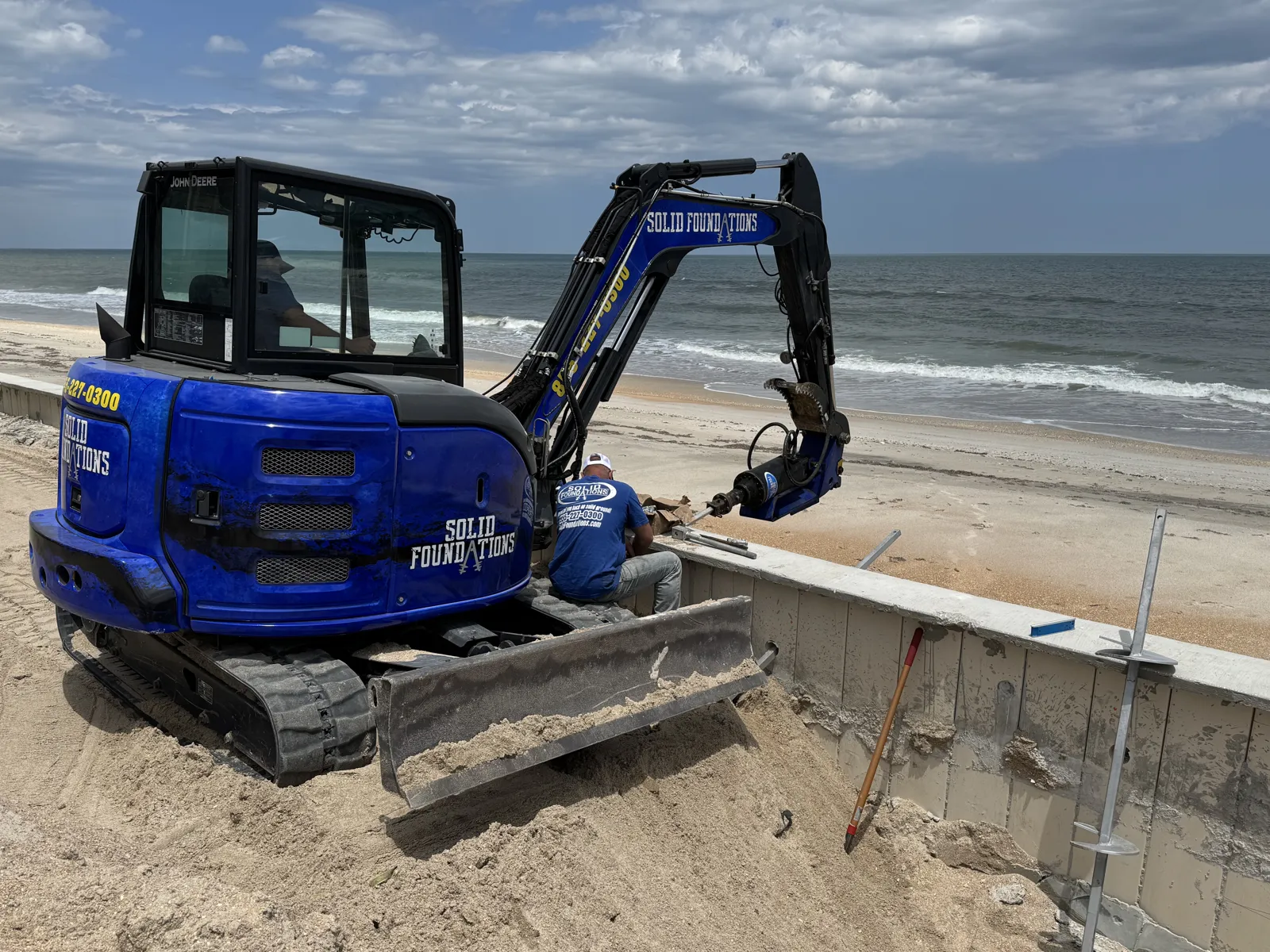 Solid Foundations crew drilling a helical tieback anchor through a concrete seawall cap