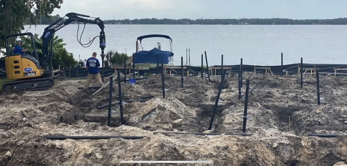Pilings being installed near the water with a boat in the background